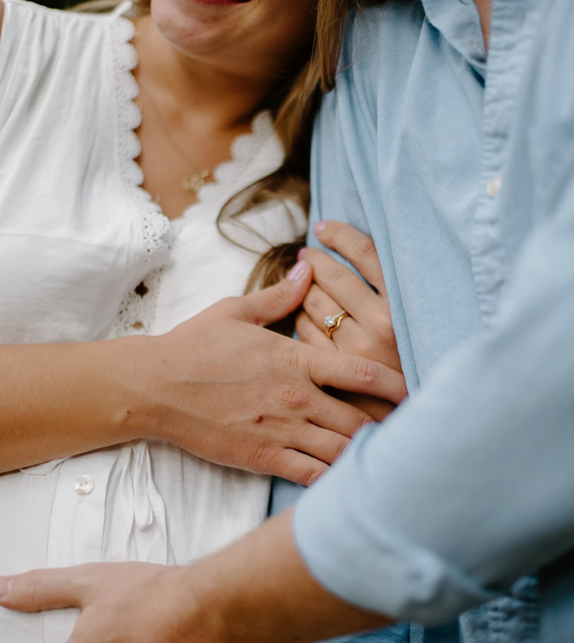 Close-up of a couple's hands, her engagement ring resting on his light blue shirt sleeve