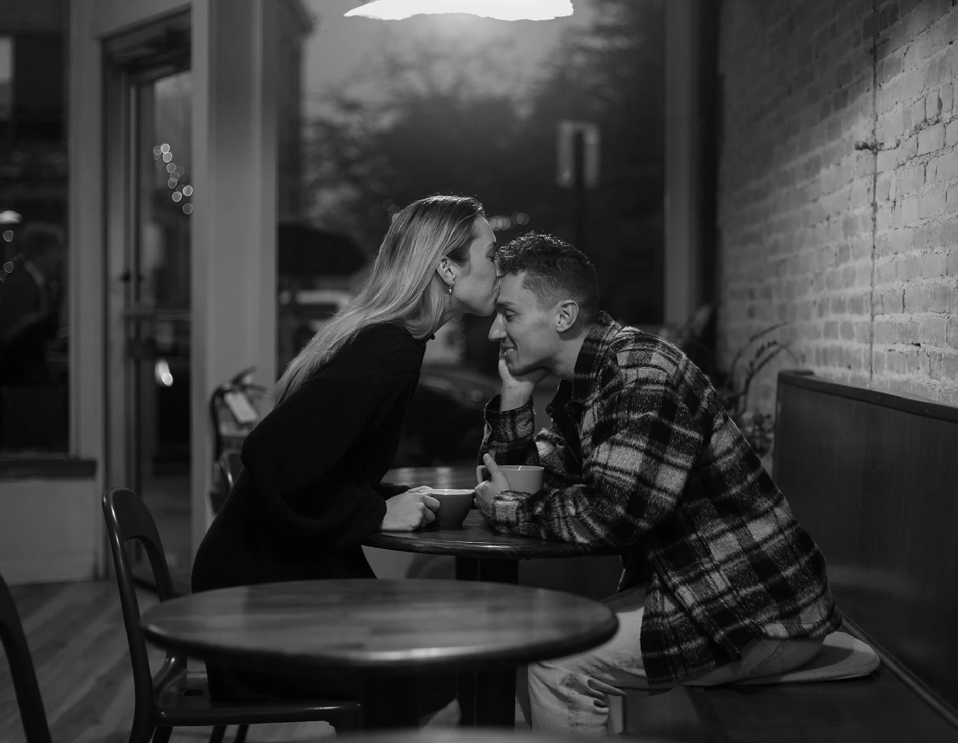 Black-and-white of Meredith kissing Gerrin's forehead at a café table