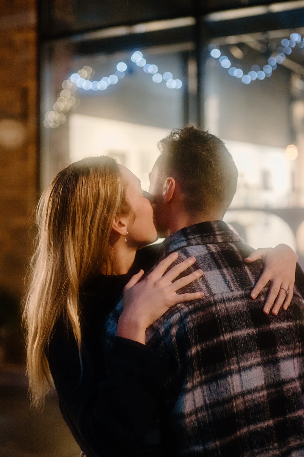 Meredith kissing Gerrin's cheek outside a lit shop window, her ring on his shoulder