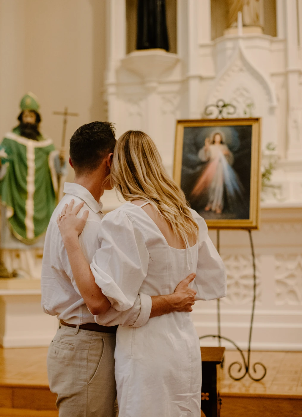 The couple from behind, arms around each other, looking toward the altar