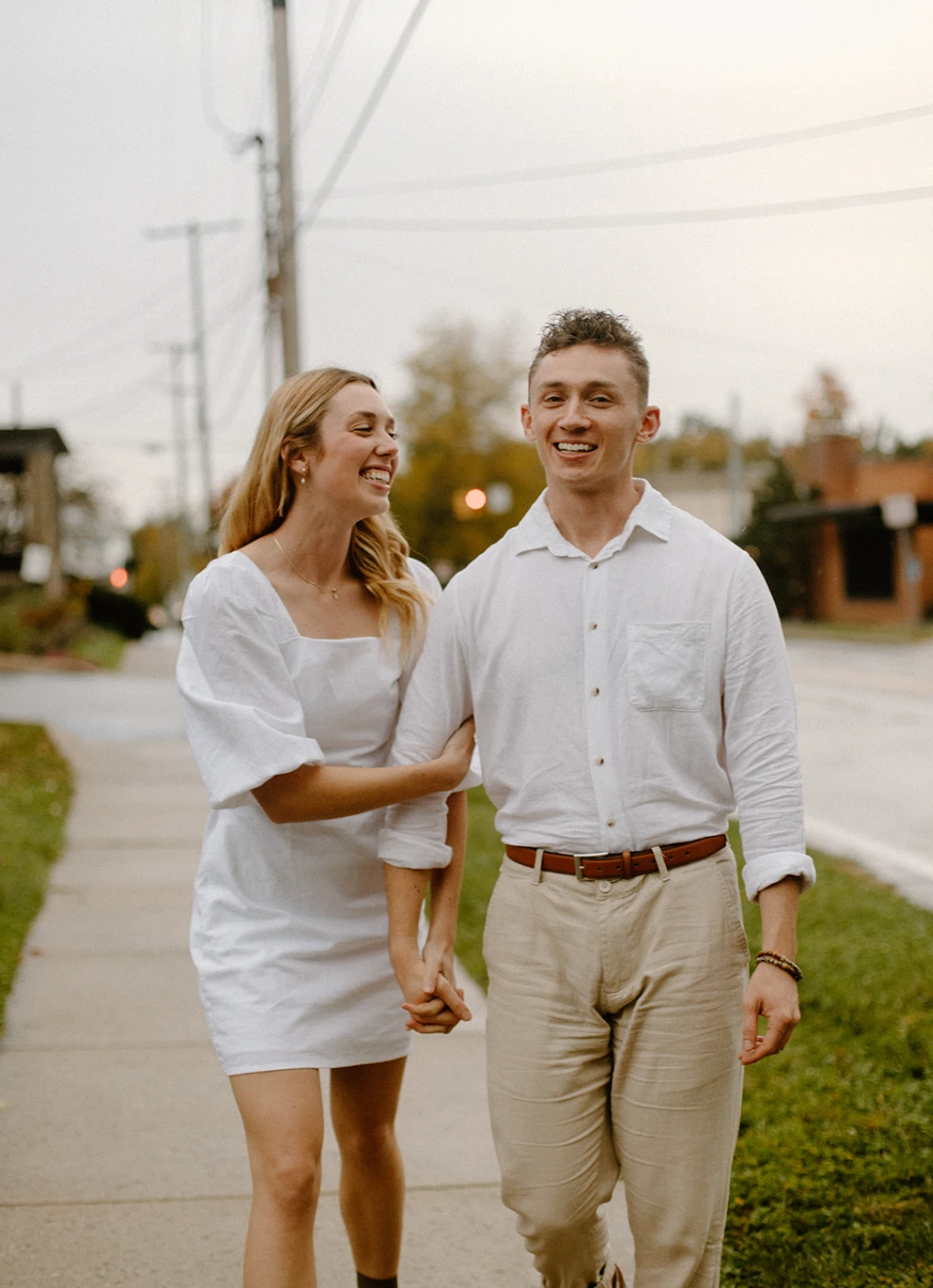 The couple walking down a sidewalk holding hands and laughing