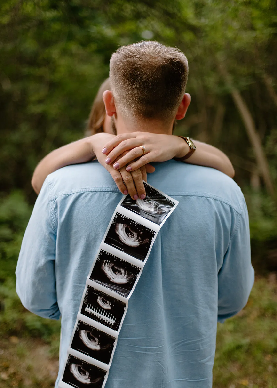 Her arms around his neck, holding a strip of ultrasound photos down his back