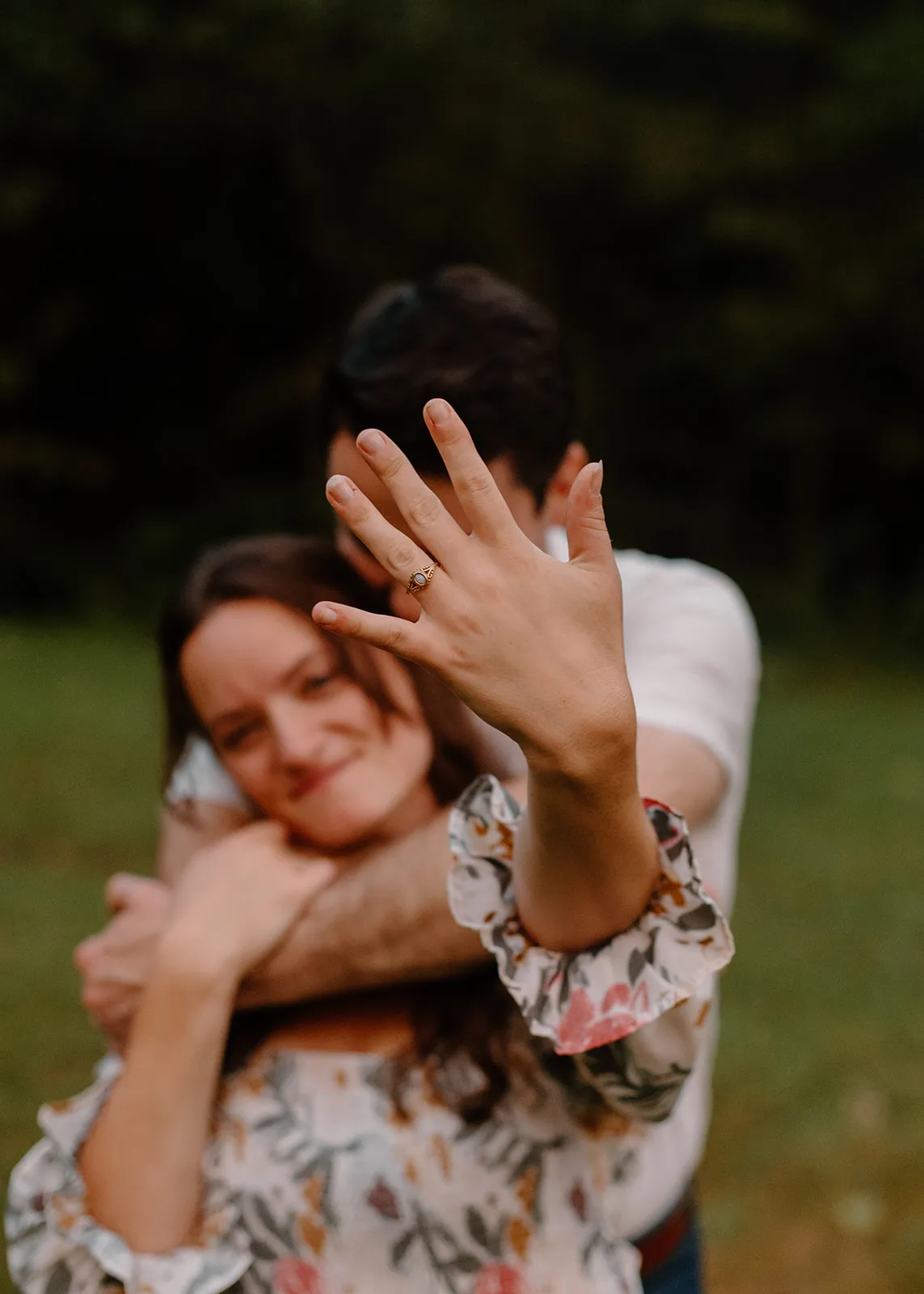 Grace showing her ring as John hugs her from behind