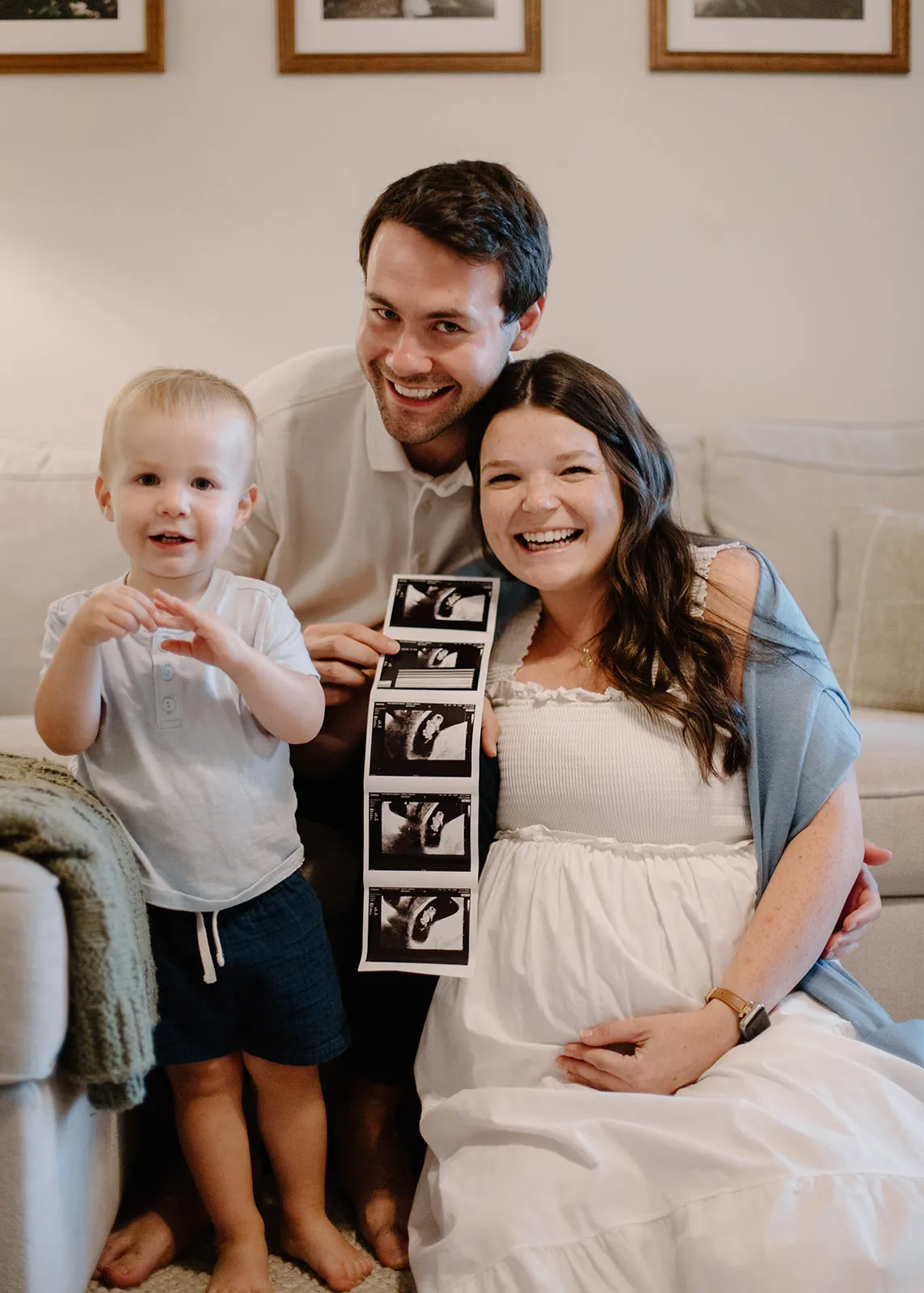 The family on the living room floor holding up a strip of ultrasound photos